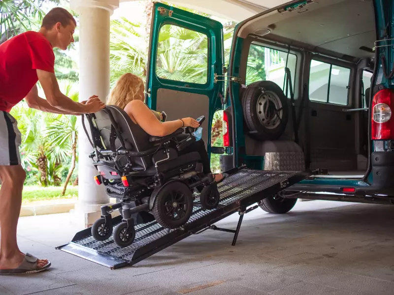 Disabled woman in wheelchair with support worker getting into van