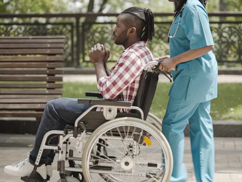 Disabled man in wheelchair outdoors with nurse