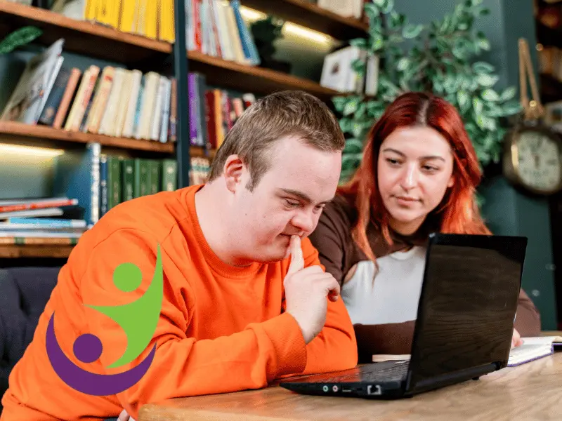 Disabled man with down syndrome using laptop with support worker